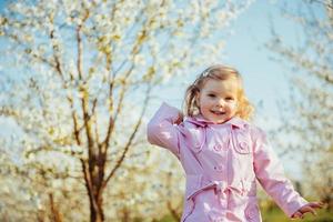 kleines Mädchen 3 Jahre, das zwischen blühenden Bäumen draußen läuft foto