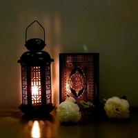 die laterne des ramadan ist schwarz, leuchtend, mit holzmotiven verziert, neben dem heiligen koran, mit ein paar weißen rosen foto