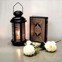 die laterne des ramadan ist schwarz, leuchtend, mit holzmotiven verziert, neben dem heiligen koran, mit ein paar weißen rosen foto