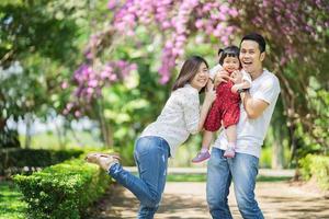schönes asiatisches Familienporträt lächelnd und glücklich. eltern werfen tochter in den garten. glückliches Familienkonzept. foto