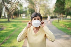 sportliche asiatische Seniorin der 60er Jahre mit OP-Maske und Joggen. Schöne ältere Asiatin, die an einem sonnigen Tag im Park läuft. foto