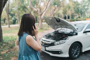 asiatische frau, die garage anruft, nachdem das auto kaputt gegangen ist. Frau, die die Motorhaube öffnet und die Versicherung oder jemanden anruft, um zu helfen, nachdem das Auto eine Panne hat, am Straßenrand parken. Transportkonzept. foto