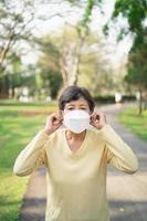 sportliche asiatische Seniorin der 60er Jahre mit OP-Maske und Joggen. Schöne ältere Asiatin, die an einem sonnigen Tag im Park läuft. foto