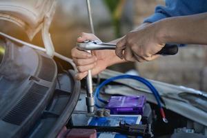 Reparatur und Einbau der Batterie. der mann zieht mit einem schraubenschlüssel die schrauben zur befestigung einer neuen batterie an und installiert ersatzteile für ein auto.