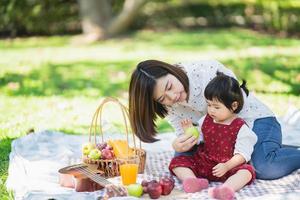 familie mit kindern, die picknick im frühlingsgarten genießen. Eltern und Kinder haben Spaß beim Mittagessen im Freien im Sommerpark. foto