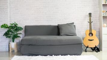 minimalistisches wohnzimmer mit sofa und gitarre auf dem boden, dekor an einer großen wand, weiße landschaft im fenster. Zuhause nordisches Interieur foto