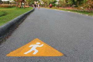 Streckensymbol zum Laufen geschrieben auf der Asphaltstraße mit verschwommenen Menschen, die im öffentlichen Park joggen.