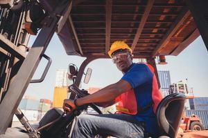 arbeiter mit helm und sicherheitsweste, die in containerstaplern sitzen, kontrollieren das laden von containern aus der fracht foto