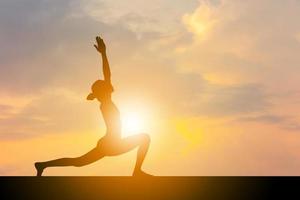 Silhouette einer jungen Frau mit Beschneidungspfad, die Yoga-Entspannungsübungen bei Sonnenuntergang praktiziert, Freiheits- und Entspannungskonzepte. foto