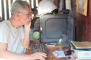 älterer asiatischer mann, der von zu hause aus mit computer arbeitet foto