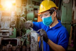 ingenieur wird inspiziert und überprüft den produktionsprozess auf der werkstation, der einen schraubendreher hält, indem er eine schutzmaske trägt, um sich vor verschmutzung und viren in der fabrik zu schützen. foto