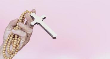 Rosenkranz mit Kreuz in der Hand auf rosa Hintergrund foto