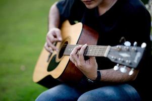 Bild eines Gitarristen, eines jungen Mannes, der Gitarre spielt, während er in einem natürlichen Garten sitzt, Musikkonzept foto