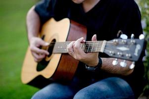 Bild eines Gitarristen, eines jungen Mannes, der Gitarre spielt, während er in einem natürlichen Garten sitzt, Musikkonzept foto