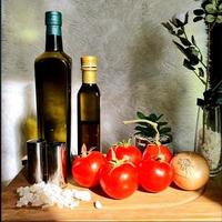 einige frische rote Tomaten und eine goldene Zwiebel auf einem Holzschneidebrett neben zwei Flaschen Öl und ein paar weißen Salzkristallen foto