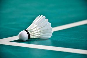 Cremeweißer Badmintonfederball und Schläger mit Neonlichtschattierung auf grünem Boden im Indoor-Badmintonplatz, verschwommener Badmintonhintergrund, Kopierraum. foto