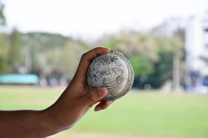 Kricketball zum Üben oder Trainieren von Hoiding in der Hand, verschwommener grüner Grasplatzhintergrund, Konzept für Cricket-Sportliebhaber auf der ganzen Welt. foto