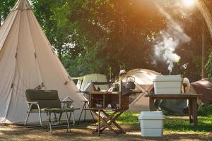 Outdoor-Küchenausstattung und Holztisch mit Feldzeltgruppe auf dem Campingplatz in einer natürlichen Parklandschaft foto