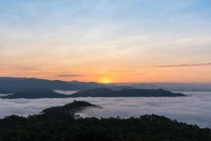 Sonnenaufgang über großen Bergen und Nebel über Wald im Winter foto