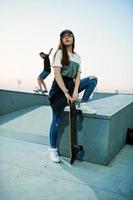 Junges urbanes Mädchen im Teenageralter mit Skateboard, Brille, Mütze und zerrissenen Jeans am Abend im Skatepark. foto