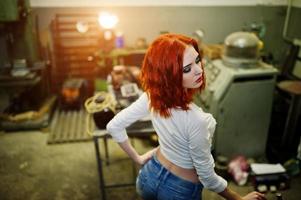 rothaarige mädchen tragen kurze jeansshorts und weiße bluse, die an der industriemaschine in der fabrik gestellt wurden. foto