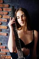Porträt eines sexy brünetten Mädchens in schwarzer Unterwäsche mit Gitarre auf industriellem Hintergrund. Model-Studio-Shooting. foto
