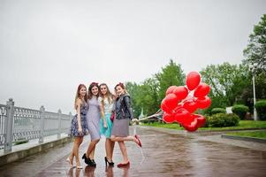 Attraktive Braut posiert mit ihren drei schönen Brautjungfern mit roten herzförmigen Luftballons auf dem Bürgersteig mit See im Hintergrund. Junggesellinnenparty. foto