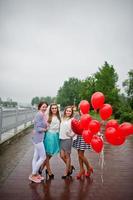 Attraktive Braut posiert mit ihren drei schönen Brautjungfern mit roten herzförmigen Luftballons auf dem Bürgersteig mit See im Hintergrund. Junggesellinnenparty. foto