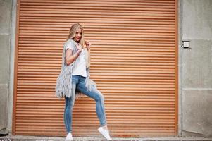 stilvolle blonde Frau trägt Jeans und Mädchen ärmellos mit weißem Hemd vor Verschlusshintergrund. Mode urbanes Modellporträt. foto