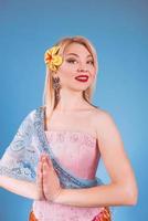 Porträt einer fröhlichen blonden europäischen Frau in thailändischer Nationaltracht, Hände namaste foto