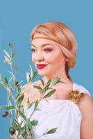 griechische blonde fröhliche frau in nationaltracht mit gefälschtem olivenzweig in ihren händen foto