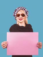 süße entzückende fröhlich lächelnde blonde frau mit sonnenbrille und arafatka mit rosa leerem tisch in ihren händen auf blauem hintergrund. Reisen foto