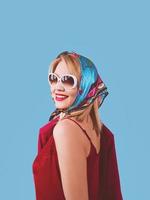 stilvolle lächelnde, fröhliche, schicke blonde Frau mit Make-up in Halstuch und Sonnenbrille auf blauem Hintergrund foto
