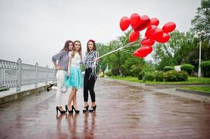 Attraktive Braut posiert mit ihren drei schönen Brautjungfern mit roten herzförmigen Luftballons auf dem Bürgersteig mit See im Hintergrund. Junggesellinnenparty. foto