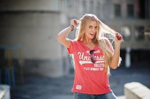 stilvolle, glückliche blonde frau trägt jeans, sonnenbrille und t-shirt, das bei sonnigem wetter auf der straße posiert. Mode urbanes Modellporträt. foto