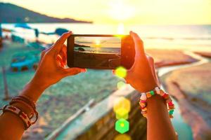asiatische frau reisen natur. Reisen entspannen. Mit dem Handy den Sonnenuntergang am Strand fotografieren. im Sommer foto