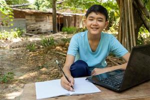 Junge, der während des Online-Unterrichts glücklich mit Laptop-Computer zu Hause auf dem Land in die Kamera schaut foto