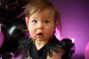 Geburtstagsfeiertag des ersten Jahres des Babymädchens. Ballons und Urlaub drinnen. Geburtstag des Kindes. kleines hübsches Mädchen in ihrem ersten schwarzen Kleid foto