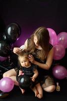 Geburtstagsfeiertag des ersten Jahres des Babymädchens. Ballons und Urlaub drinnen. Geburtstag des Kindes. kleines hübsches Mädchen mit ihrer Mutter im schwarzen Kleid foto
