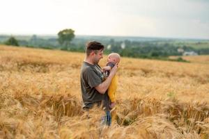 Ein junger Vater hält seinen drei Monate alten Sohn in den Armen. in einem Weizenfeld gefilmt. foto