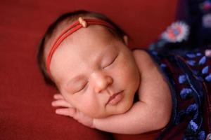 neugeborenes mädchen, das auf einem roten tuch in einer roten hülle schläft foto