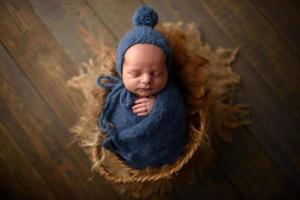 neugeborener junge in einer blauen strickmütze und wicklung schläft in einem korb auf einem hölzernen hintergrund. foto