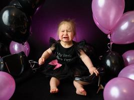 Geburtstagsfeiertag des ersten Jahres des Babymädchens. Ballons und Urlaub drinnen. Geburtstag des Kindes. kleines hübsches Mädchen in ihrem ersten schwarzen Kleid foto