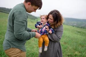 Mama, Papa und Tochter. eltern halten baby an den händen und gehen auf die kamera zu. foto