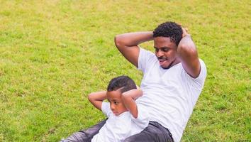 fröhlicher afroamerikanischer vater und sohn, die im park trainieren, glücksfamilienkonzepte foto