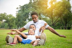 fröhlicher afroamerikanischer vater und zwei söhne spielen im park, glücksfamilienkonzepte, eltern und kinder spielen im park foto