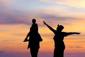 Silhouette von glücklichem Vater, Mutter und Tochter, die zusammen im Freien spielen, fröhliche Familie, die bei Sonnenuntergang genießt, glückliche Familienkonzepte foto