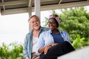 Fröhliche afroamerikanische Frau und ein älterer asiatischer Mann sitzen auf der Terrasse und schauen in die Kamera foto