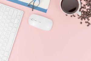 Draufsicht mit Kopierraum der Kaffeetasse mit Kaffeebohnen Computertastatur und Maus über dem Kopf auf rosa Pastellhintergrund, flaches Laienkonzept foto