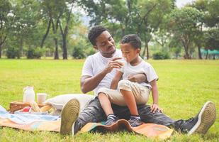 fröhlicher afroamerikanischer vater und sohn beim picknick im park, glücksfamilienkonzepte foto